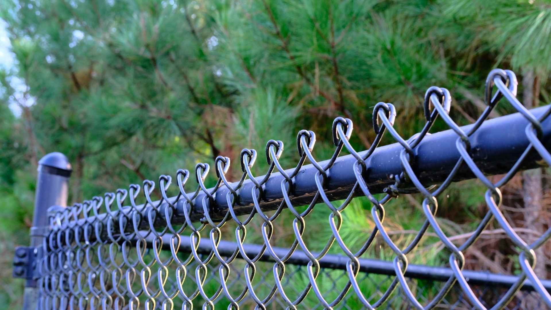Blogs 10 Technician tightening chain link fence fabric on backyard line at Quality Fence Inc